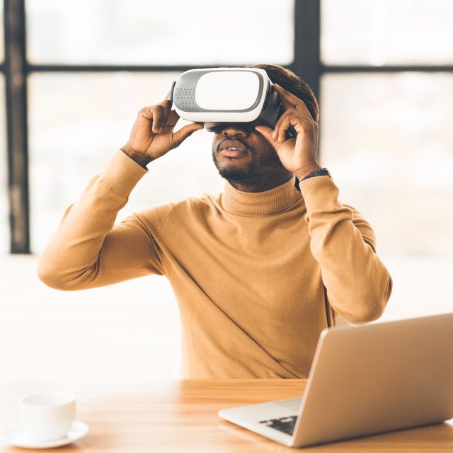 Afro Businessman Wearing Augmented Reality Goggles At Home